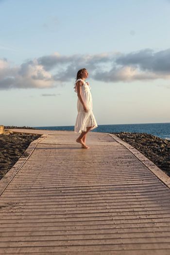 Side view of girl standing on boardwalk against sea