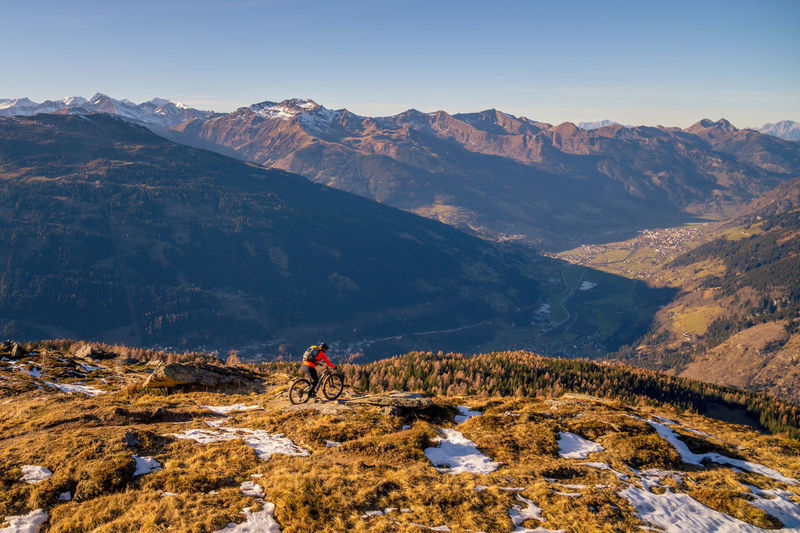 Woman riding a mountain bike on footpath in snow covered alpine terrain, gastein, salzburg, austria.