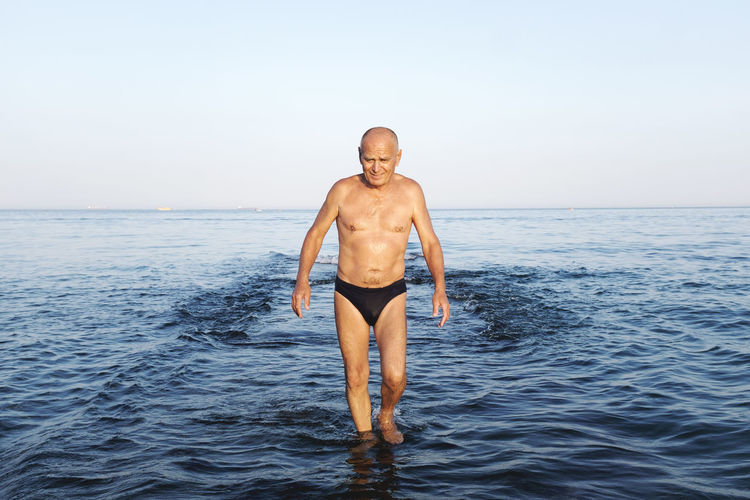 Shirtless man wading in sea against sky