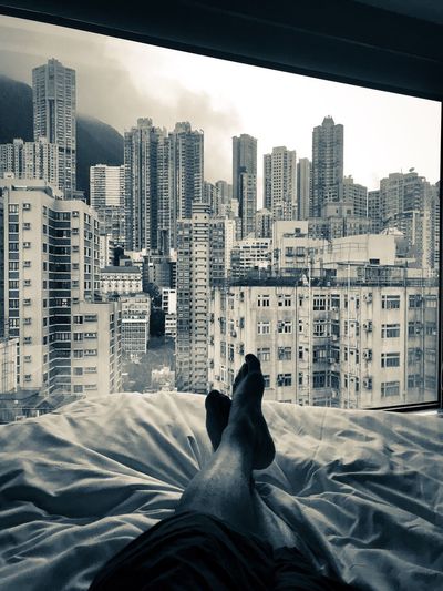 Low section of man relaxing on bed against buildings in city