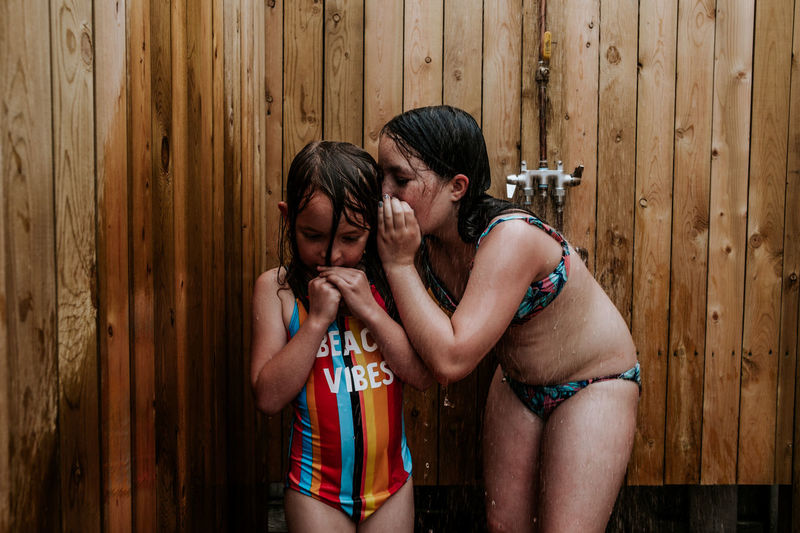 Sister whispering in younger sister's ear in outdoor shower