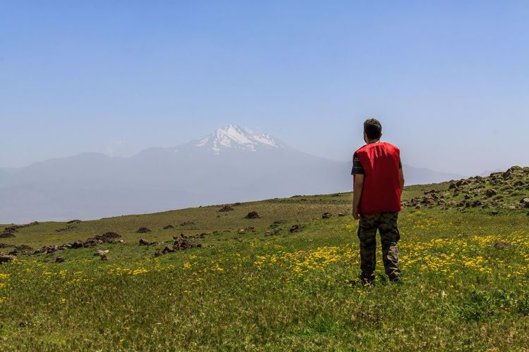 Rear view of man standing on field against clear sky