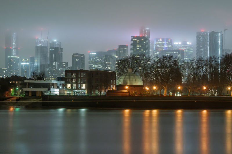 Illuminated city by river against sky at night