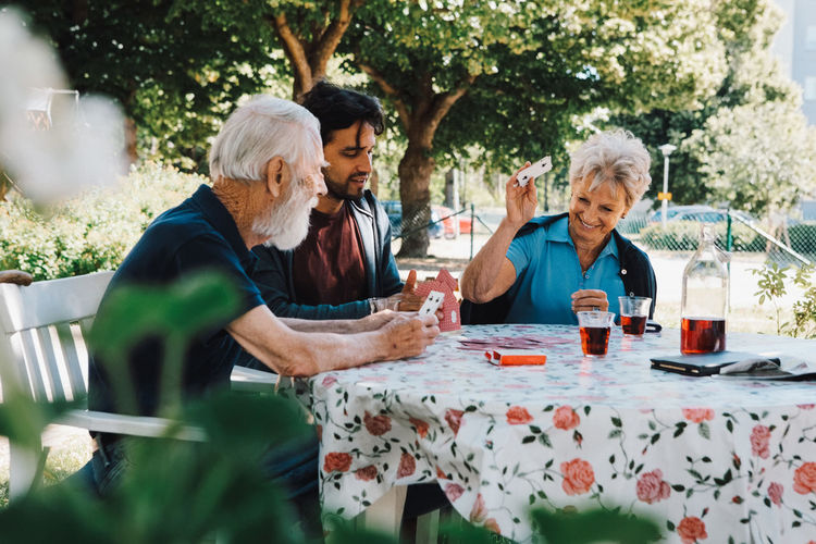 Cheerful senior woman playing cards with males at table in back yard