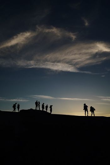 Silhouette people on land against sky during sunset
