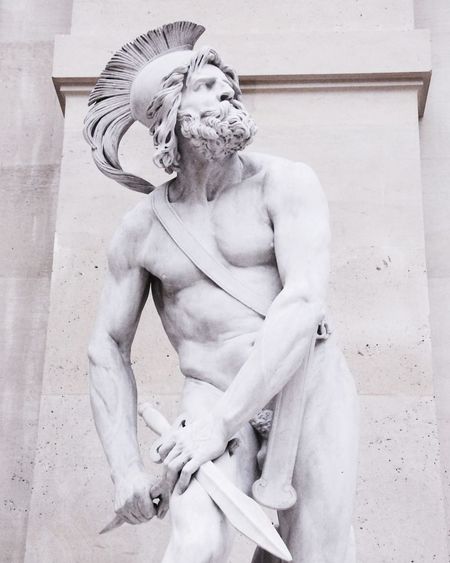 Statue of man sitting against white wall