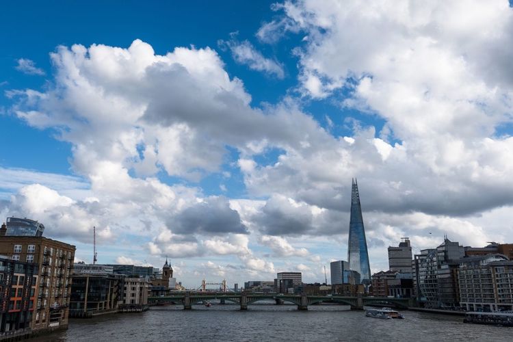 The shard in city by thames river against cloudy sky