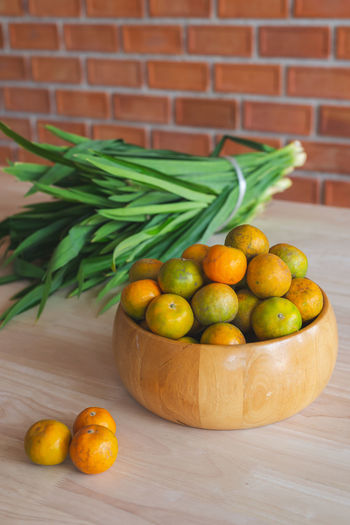 Fresh orange in the wooden bowl put on the wooden table with the pandanus behind.