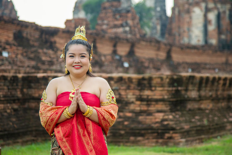 Portrait smiling asian woman in a thai dress pay respect with an old pagoda background