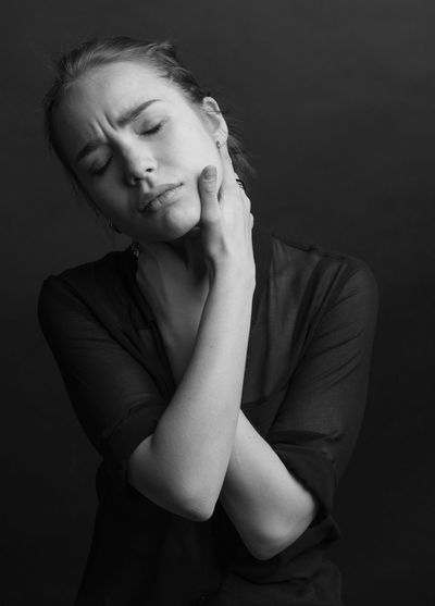 Young woman touching neck against black background
