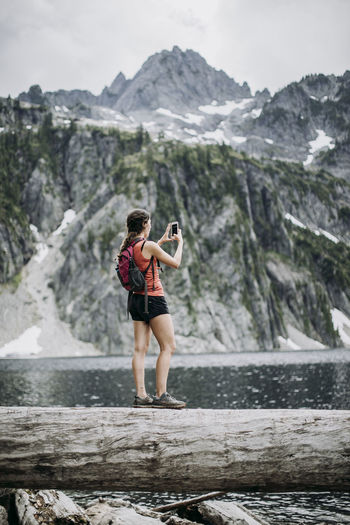 A female hiker takes a cell photo picture while hiking along a lake