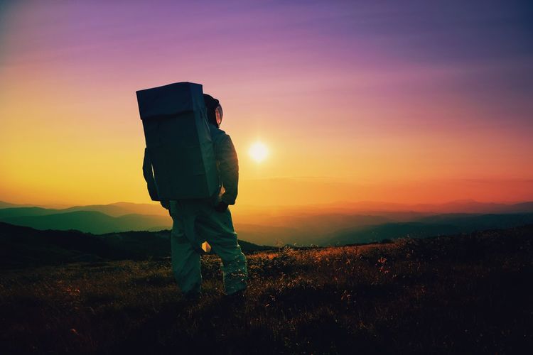 An astronaut standing on field against sky during sunset