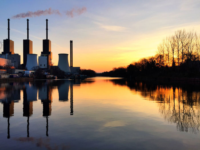 Smoke stack emitting pollution from power plant with reflection during sunset