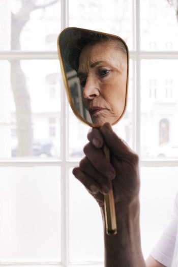 Reflection of worried senior woman in mirror at home