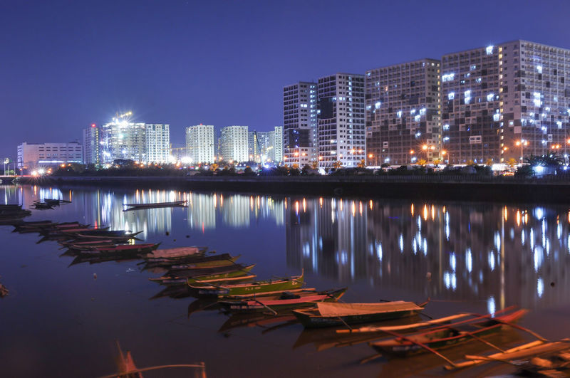 Illuminated buildings by lake against sky in city at night