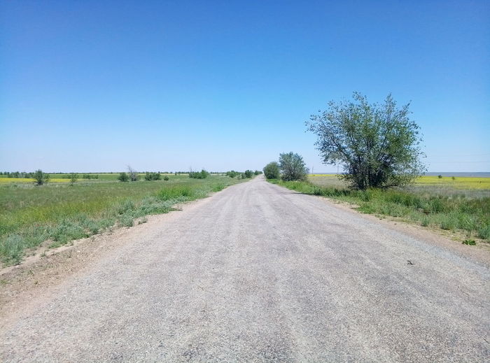 Road amidst field against clear blue sky