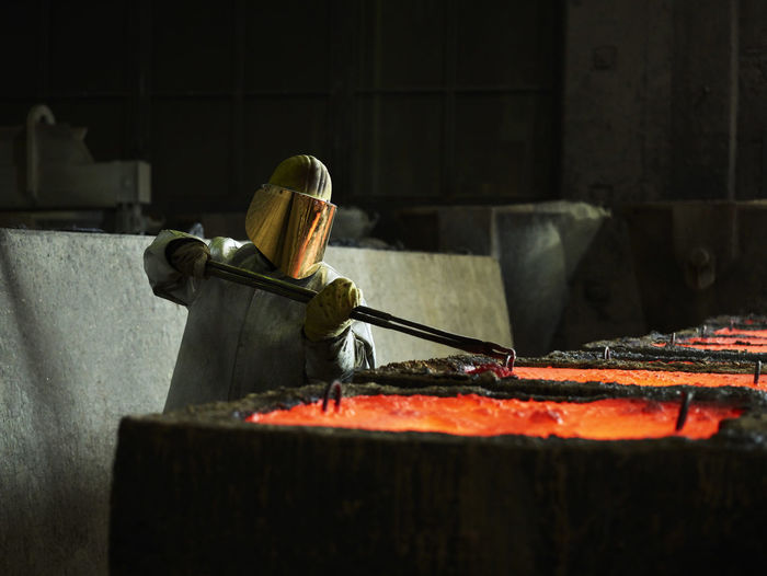 Industry, worker checking liquid copper in casting moulds with pliers