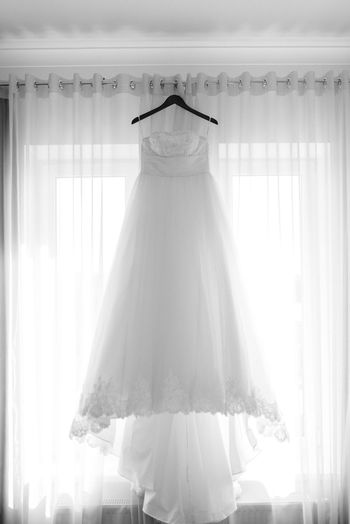 Front view of wedding dress hanging against white curtain