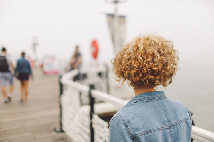 Rear view of young woman standing by railing on brighton pier