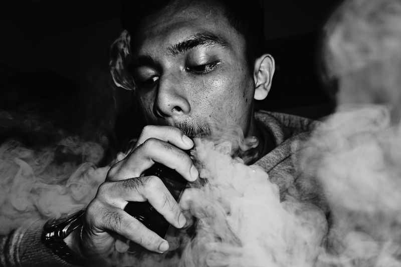 Close-up of man smoking against black background