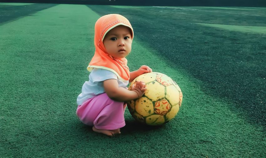 Cute girl with ball crouching on field