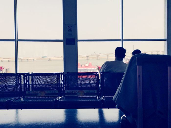 Rear view of man sitting on window at airport