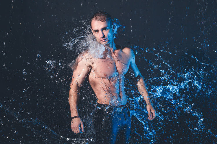 Portrait of shirtless man standing against black background