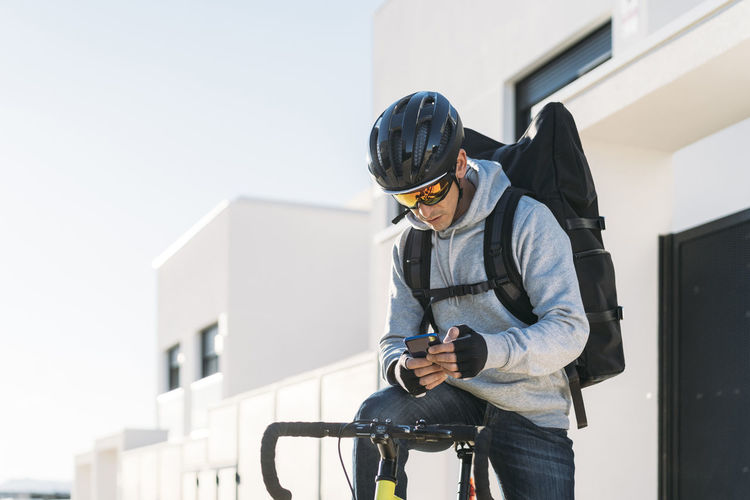 Delivery man with bicycle using smart phone on sunny day