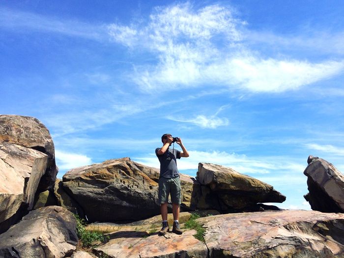 Man photographing through camera while standing on rock against sky