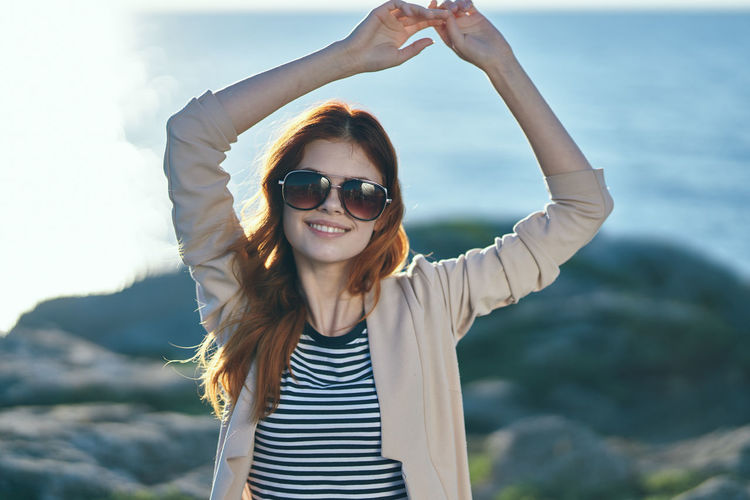 Portrait of young woman wearing sunglasses standing against sky