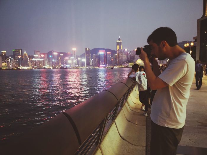 Side view of man photographing illuminated cityscape at night
