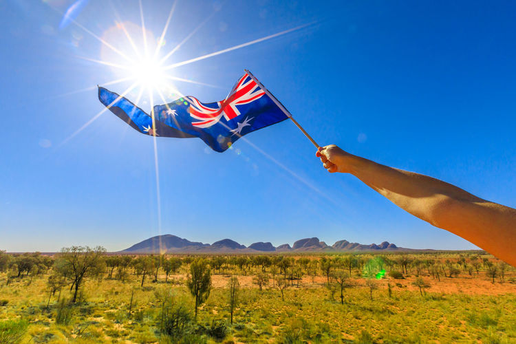 Cropped hand of person holding australian flag against clear blue sky