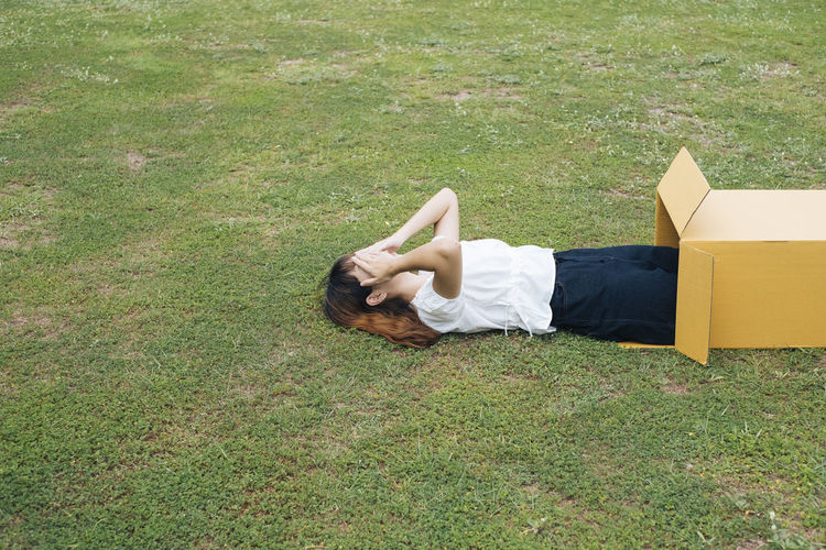 Woman lying on grass in cardboard box