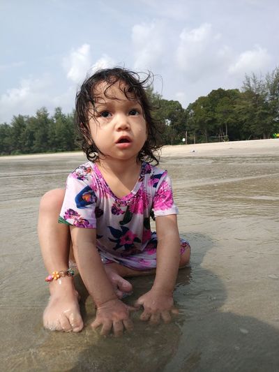 Cute girl sitting in sea against sky