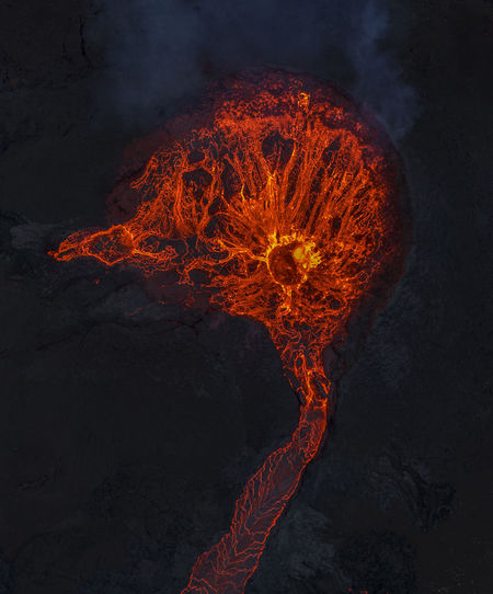 Drone view of stream of hot orange lava flowing through mountainous terrain in morning in iceland