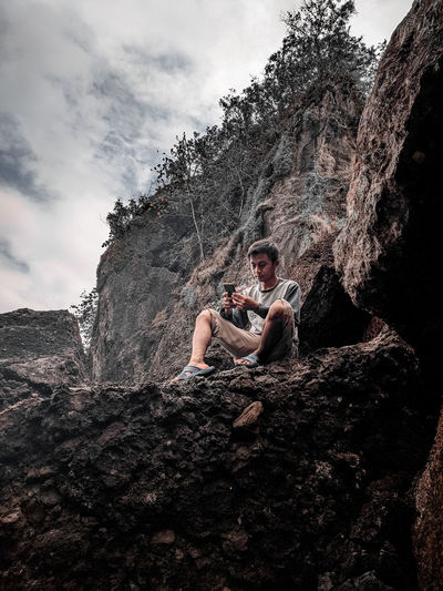 Low angle view of man sitting on rock