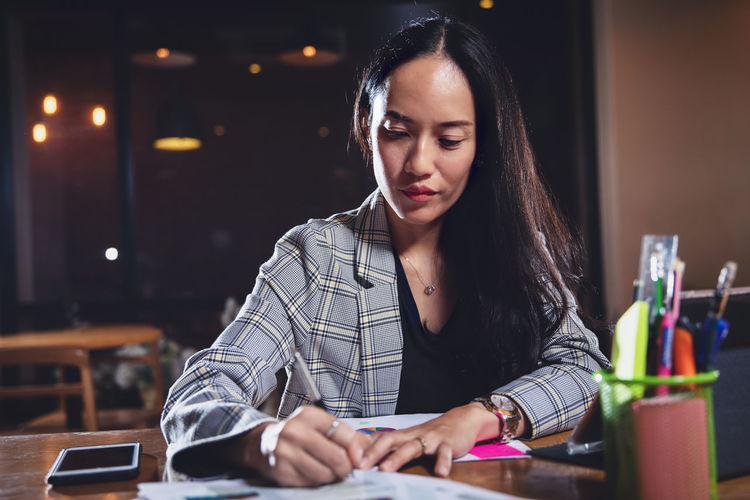 Businesswoman writing on document while sitting in office