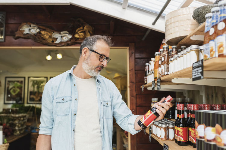 Mature man checking bottle while shopping in store