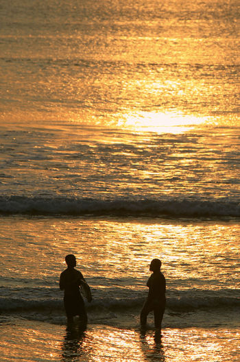 Silhouette friends standing at beach during sunset