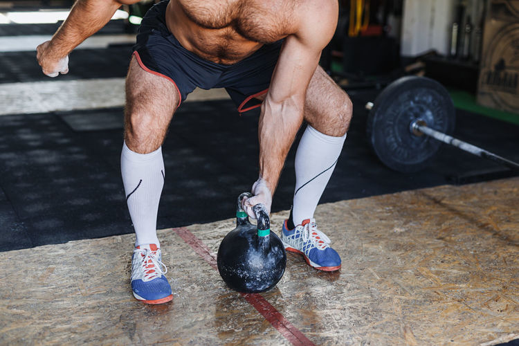 Low section of man lifting kettlebell while exercising in gym