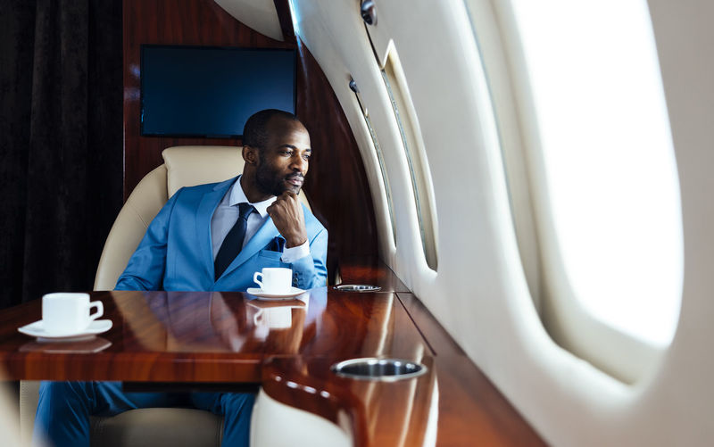Young businessman with hand on chin looking through window while sitting in private jet