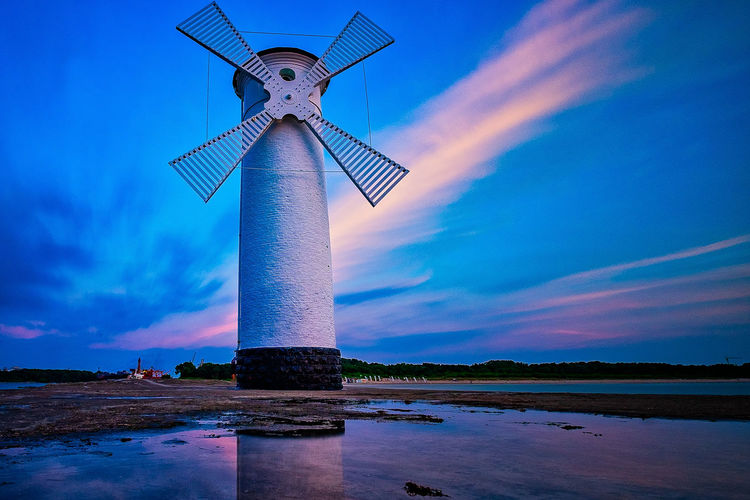 Traditional windmill at beach against sky during sunset