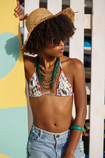 Young beautiful woman wearing sunglasses standing next to the surfboard