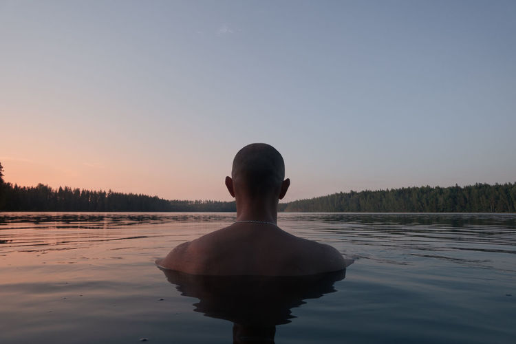 A man swims in a forest lake in the evening. back view. alone with nature.
