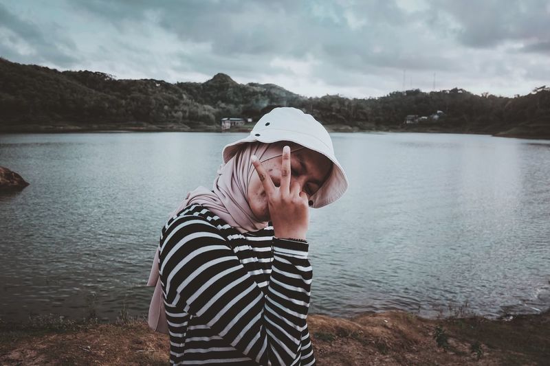 Woman gesturing while standing by lake
