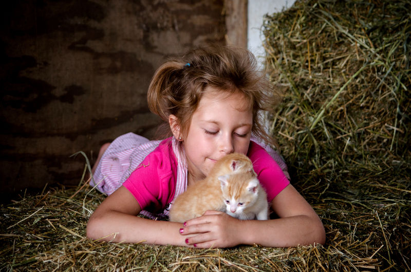 Young farm girl in pink overalls, cuddles with kittens in the barn, on bales of straw