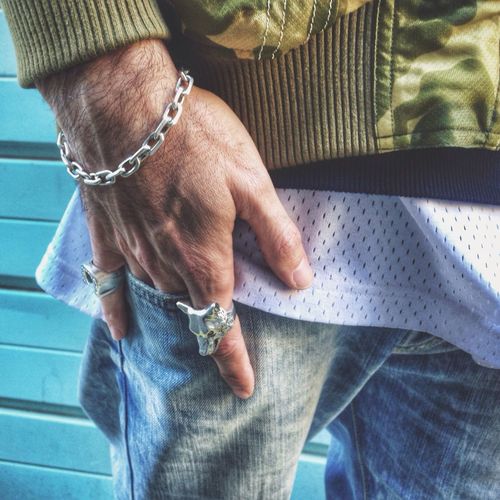 Mid section of man with rings and metal bracelet holding hand in pocket