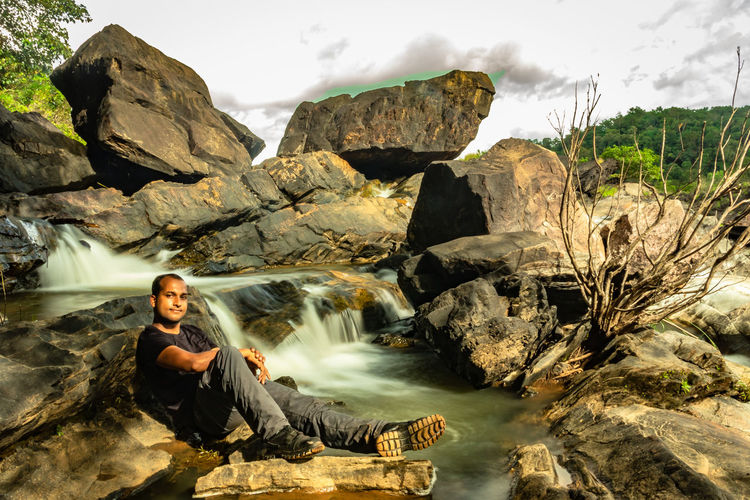 Portrait of man sitting on rock against waterfall