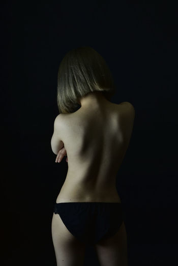 Rear view of shirtless young woman against black background