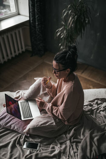 High angle view of woman using laptop sitting on bed at home